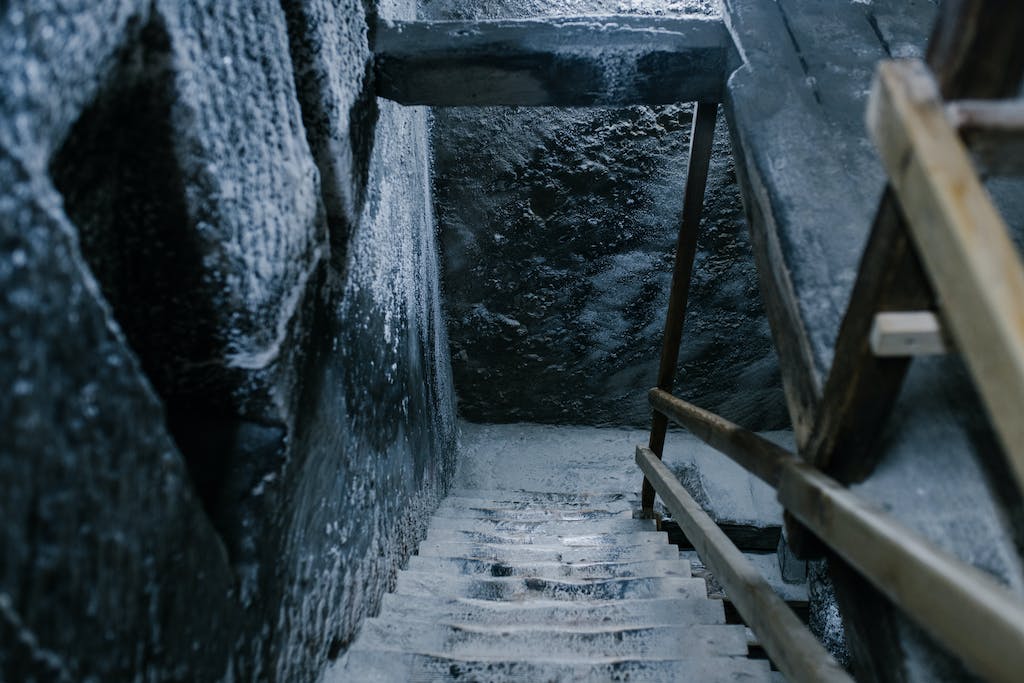 From above of aged stone stairway covered with salt in ancient cave with shabby walls and wooden railings in Registry Chamber of Salina Turda mine